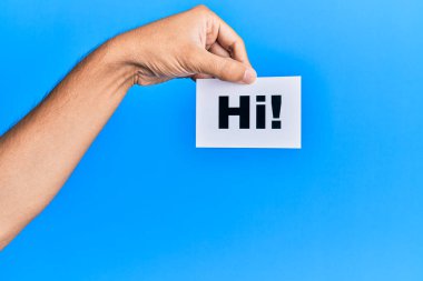 Hand of caucasian man holding paper with hi! greeting over isolated blue background