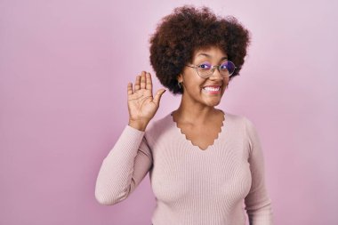Young african american woman standing over pink background waiving saying hello happy and smiling, friendly welcome gesture 