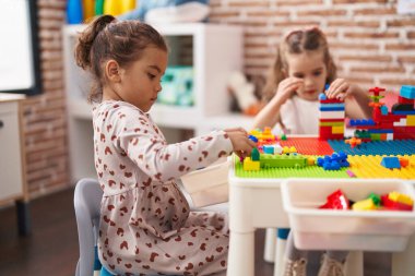 Two kids playing with construction blocks sitting on table at kindergarten