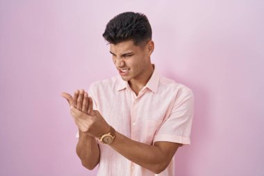 Pembe arka planda duran genç İspanyol adam ellerinde ve parmaklarında ağrı, eklem iltihabı 