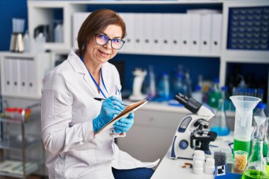 Laboratuvarda not defterine yazan orta yaşlı kadın bilim adamı.