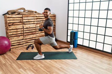 Genç Arap adam gülümsüyor spor merkezinde kettlebell ile antrenman yapıyor.