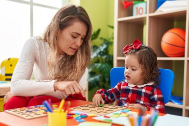 Teacher and toddler playing with maths puzzle game sitting on table at kindergarten