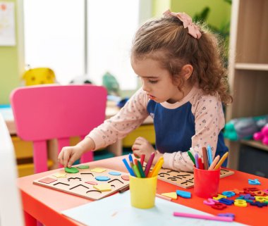 Adorable blonde girl playing with maths puzzle game sitting on table at kindergarten