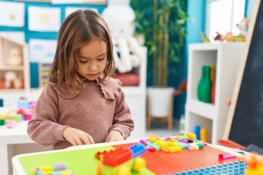 Anaokulundaki masada oturan, inşaat bloklarıyla oynayan sevimli İspanyol kız.