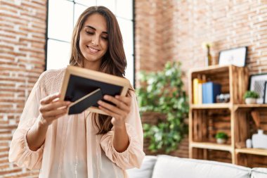 Young hispanic woman smiling confident holding picture at home