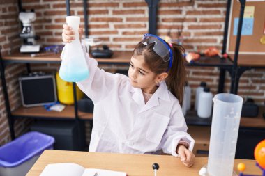 Adorable hispanic girl student holding test tube at laboratory classroom