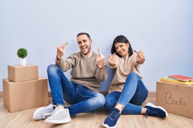 Young couple moving to a new home showing middle finger doing fuck you bad expression, provocation and rude attitude. screaming excited 