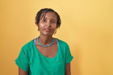 African woman with dreadlocks standing over yellow background looking sleepy and tired, exhausted for fatigue and hangover, lazy eyes in the morning. 
