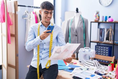 Genç İspanyol terzi, terzi dükkanında elbise tasarımına akıllı telefondan fotoğraf çekiyor.