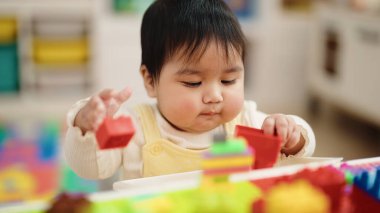 Adorable hispanic baby playing with construction blocks sitting on table at kindergarten