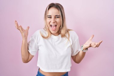 Pembe arka planda duran genç sarışın kadın çılgın ve başarıyı kollarını kaldırıp heyecanla haykırarak kutluyor. Kazanan konsept 