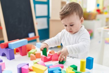 Sevimli beyaz bebek anaokulunda duran inşaat bloklarıyla oynuyor.