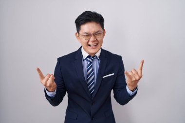 Young asian man wearing business suit and tie shouting with crazy expression doing rock symbol with hands up. music star. heavy music concept. 