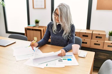 Ofiste çalışırken gülümseyen beyaz saçlı iş kadını.