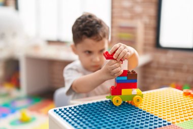 Adorable hispanic toddler playing with construction blocks sitting on table at kindergarten