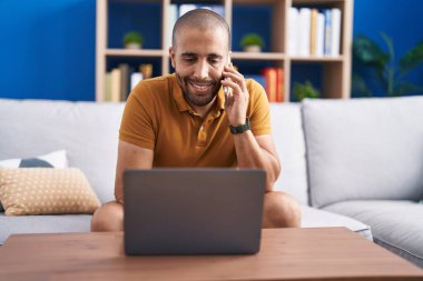 Genç latin adam akıllı telefonda dizüstü bilgisayar kullanarak konuşuyor.