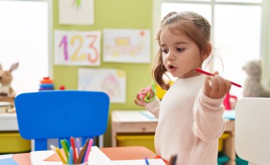 Adorable hispanic girl playing with toys standing at kindergarten