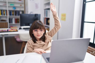 Adorable hispanic girl student having lesson with hand raised up at classroom