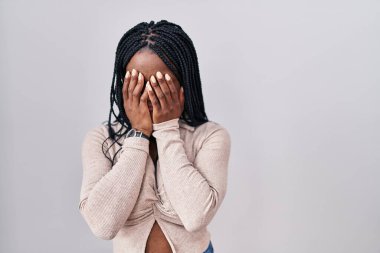 African woman with braids standing over white background with sad expression covering face with hands while crying. depression concept. 