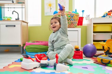 Adorable hispanic toddler playing with supermarket toy sitting on floor at kindergarten