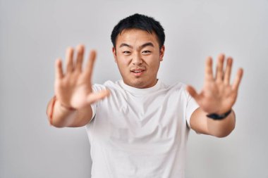 Young chinese man standing over white background doing stop gesture with hands palms, angry and frustration expression 