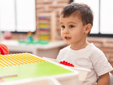 Anaokulundaki masada oturan, inşaat bloklarıyla oynayan sevimli çocuk.