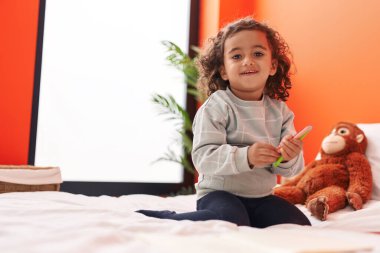 Adorable hispanic girl holding color pencils sitting on sofa at bedroom