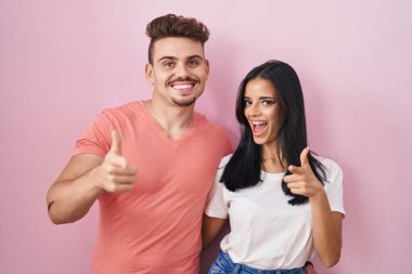 Young hispanic couple standing over pink background pointing fingers to camera with happy and funny face. good energy and vibes. 