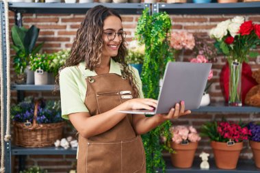 Young beautiful hispanic woman florist smiling confident using laptop at flower shop