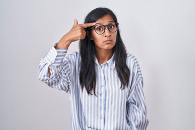 Young hispanic woman wearing glasses pointing unhappy to pimple on forehead, ugly infection of blackhead. acne and skin problem 