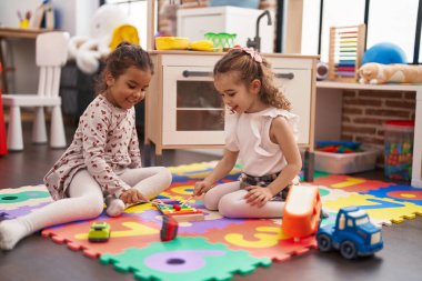 Two kids playing xylophone sitting on floor at kindergarten