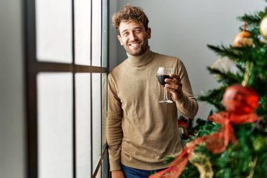 Genç İspanyol adam evde Noel ağacının yanında şarap içiyor.