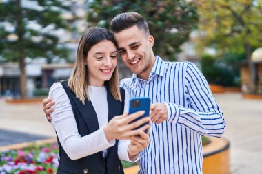 Man and woman couple hugging each other using smartphone at park