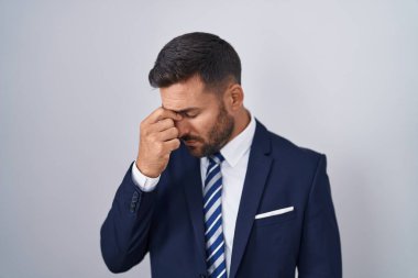 Handsome hispanic man wearing suit and tie tired rubbing nose and eyes feeling fatigue and headache. stress and frustration concept. 