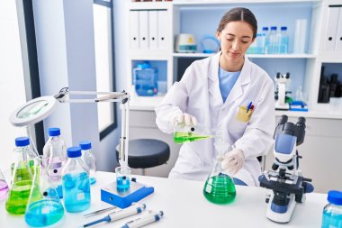 Genç ve güzel İspanyol bilim kadını laboratuarda test tüpüne sıvı döküyor.