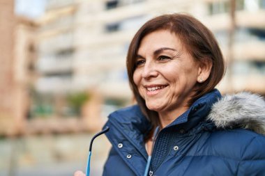 Orta yaşlı bir kadın elinde bardaklarla caddeye bakıyor.