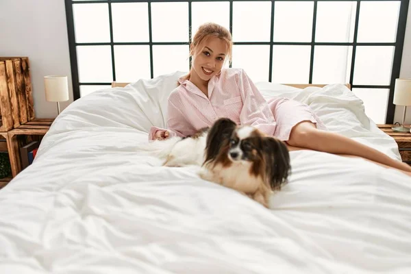 Young caucasian woman smiling confident lying on bed with dog at bedroom