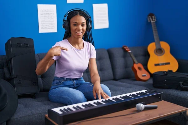非洲裔美国妇女 辫子在音乐工作室弹钢琴 手指对着一个快乐而自豪的自我微笑 — 图库照片