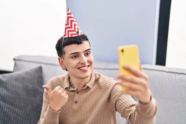 Non binary person celebrating birthday doing video call pointing thumb up to the side smiling happy with open mouth