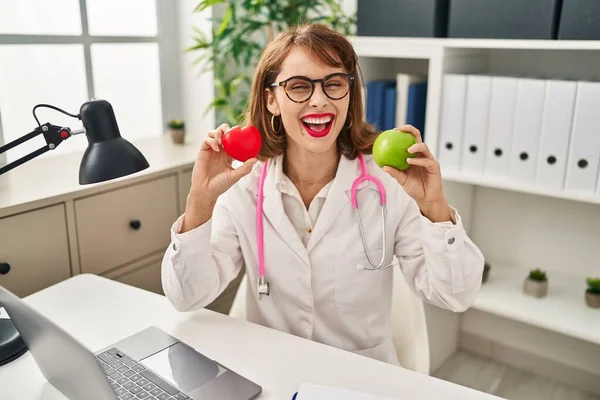 Young Doctor Woman Holding Heart Green Apple Smiling Happy Cool — стоковое фото