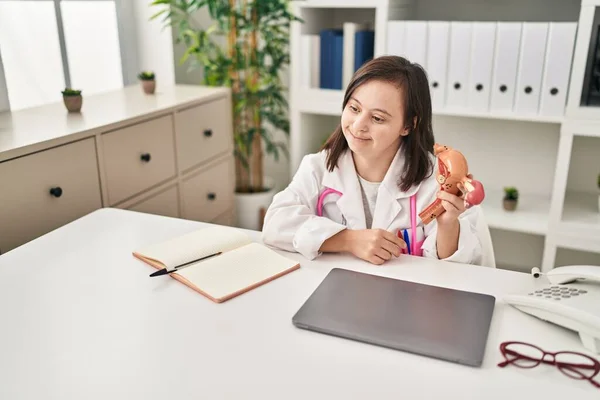 Down syndrome woman wearing doctor uniform holding anatomical model of uterus at clinic