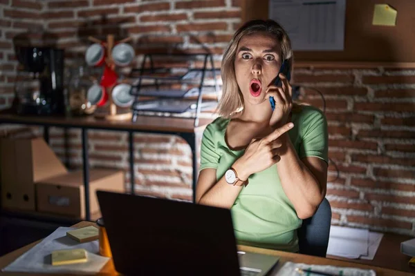 Young Beautiful Woman Working Office Night Speaking Phone Surprised Pointing — Stockfoto