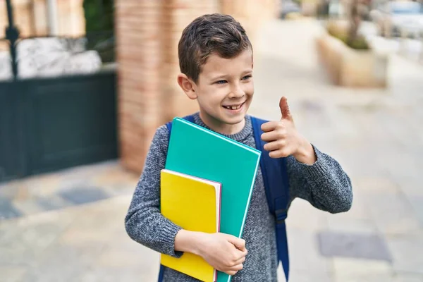 Blond child student holding books doing ok gesture at street