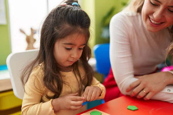 幼儿园的老师和幼儿坐在桌子上玩数学拼图游戏 — 图库照片