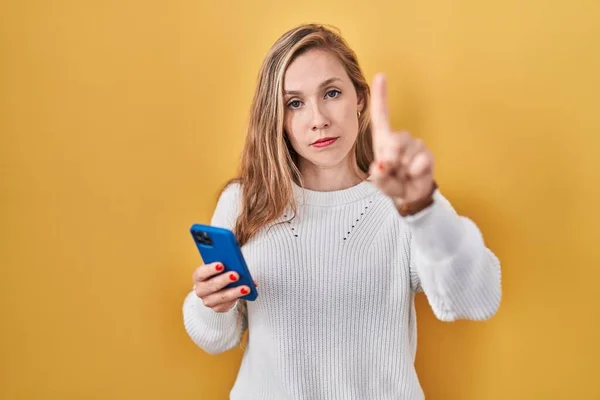 Молодая Блондинка Использующая Смартфон Печатает Сообщение Показывая Пальцем Вверх Злое — стоковое фото