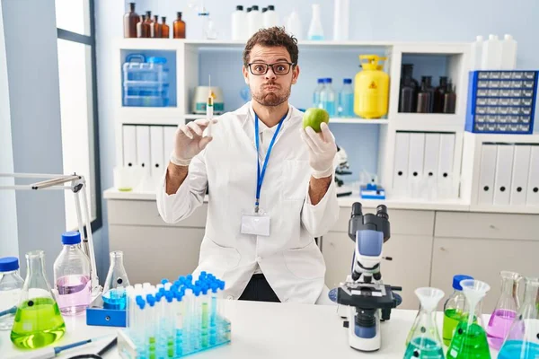 Young Hispanic Man Working Scientist Laboratory Holding Apple Puffing Cheeks — Photo