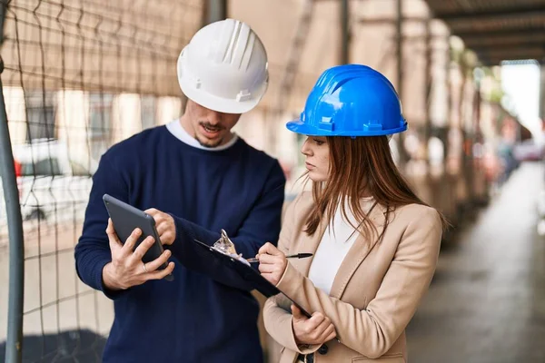 Mand and woman architects using touchpad write on report at street