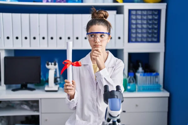 Teenager Girl Working Scientist Laboratory Holding Degree Serious Face Thinking — Stockfoto