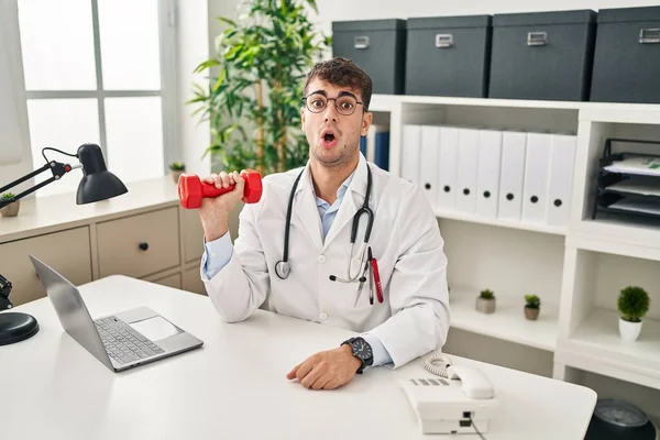 Young Hispanic Doctor Man Holding Dumbbells Scared Amazed Open Mouth — Stockfoto